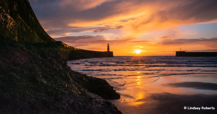 Sunrise with orange and pink sky over Slope Beach and a lighthouse at Seaham County Durham.